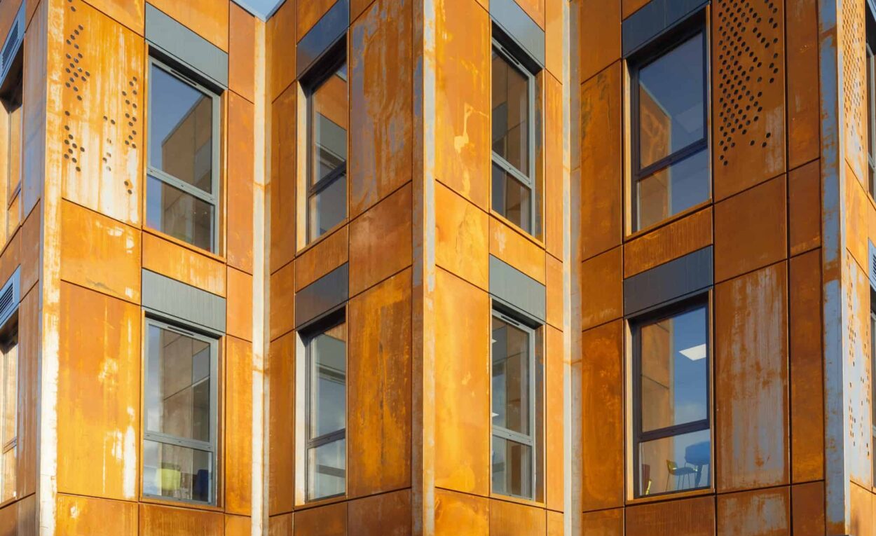 Outside view of Modular building coated in aluminium powder. Multiple modular classrooms, in a zigzag shape, onto podiums that leave room for car parking.